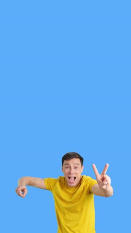 man in yellow shirt making victory sign on blue background