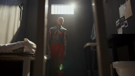 shirtless tattooed inmate wandering around prison cell on boring day