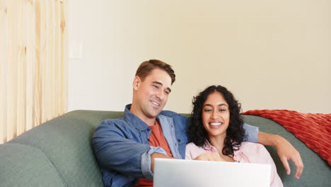 smiling multiracial couple sitting on couch, watching something on laptop, at home, copy space