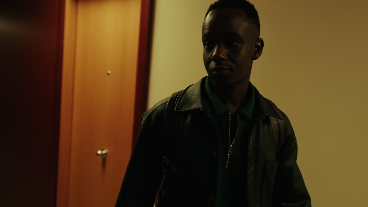 Jovem negro caminhando por um corredor escuro de hotel.