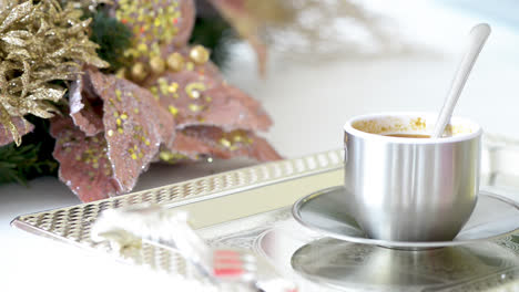 cup of cappuccino with spoon on silver tray in kitchen decorated for christmas