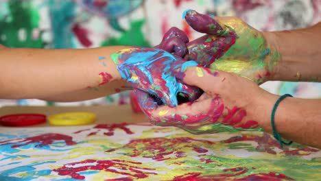 Un-Adulto-Sostiene-Las-Manos-De-Un-Niño-Con-Pintura-Azul-Y-Roja.