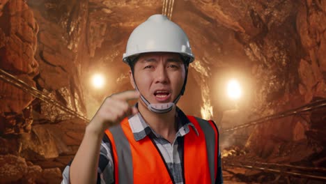 close up of angry asian male engineer with safety helmet shouting at someone while standing in underground mine tunnel
