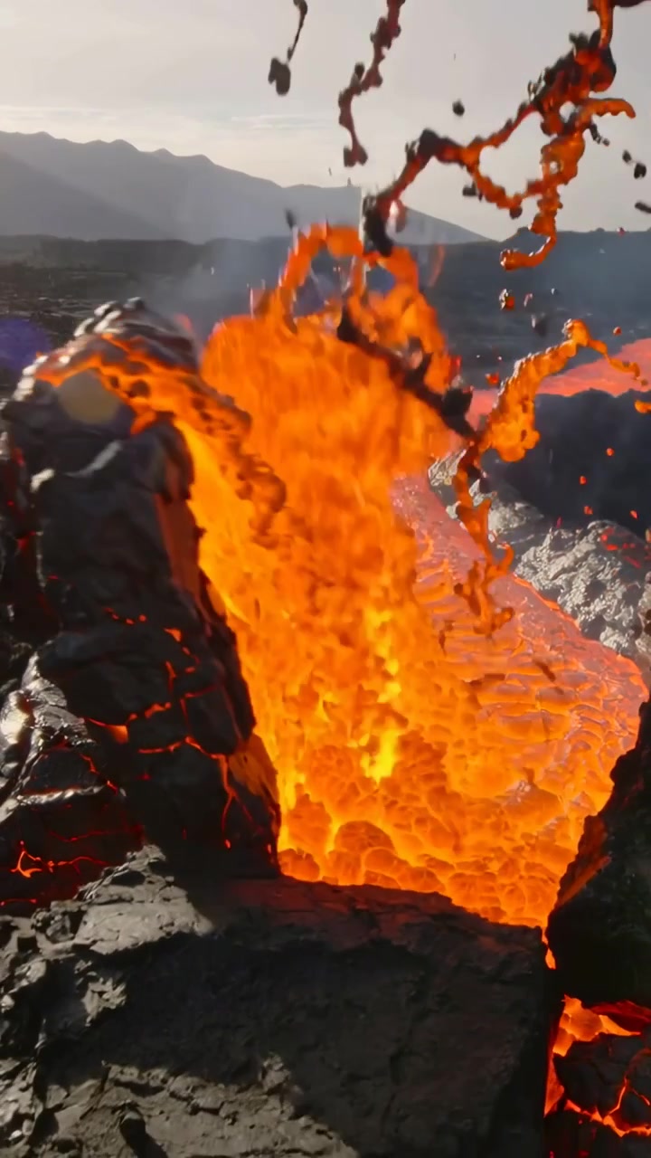 Vertical video: Surging lava cracking crust and throwing glowing droplets on lava field from magma