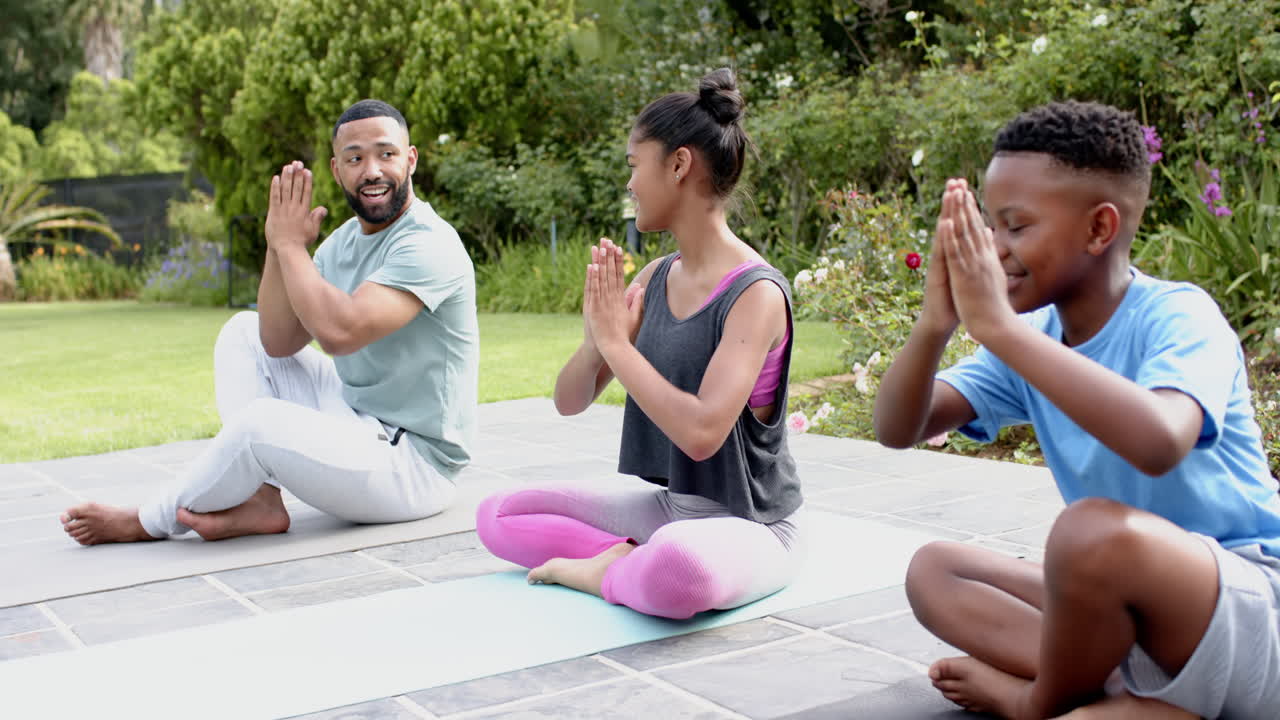 African american father teaching son and daughter yoga meditation sitting in garden, slow motion
