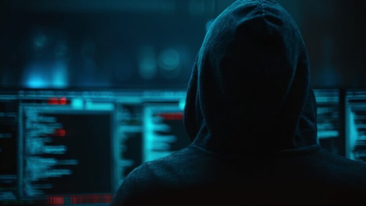 En mystisk figur fordybet i den digitale verden, omgivet af glødende skærme med kode og data i et mørklagt miljø.