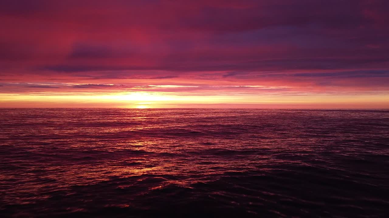 발트해의 아름다운 공중 생생한 고대비 분홍색 보라색 일몰, 카로스타 전쟁 항구 콘크리트 해안 요새 폐허 리파자, 넓은 각도의 드론 샷이 잔잔한 바다 위로 낮게 뒤로 이동