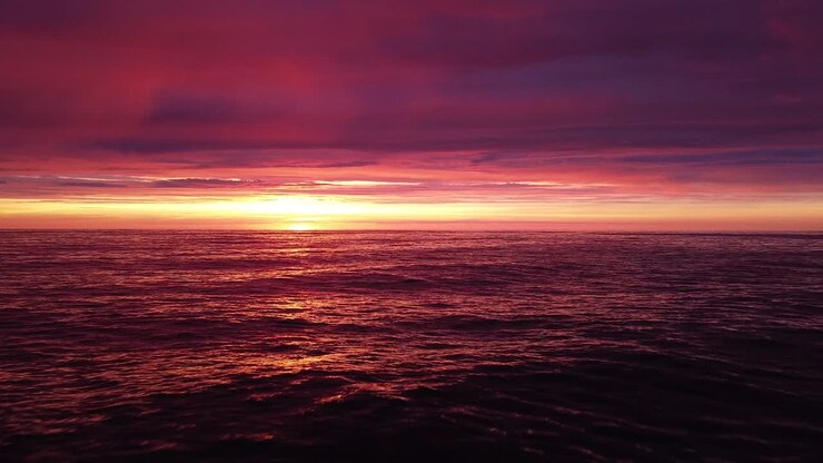 Beautiful aerial vibrant high contrast pink purple sunset over Baltic sea, Karosta war port concrete coast fortification ruins at Liepaja, wide angle drone shot moving backwards low over the calm sea