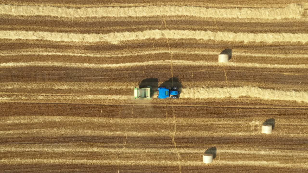 Aerial view of tractor tow trailed bale machine to collect straw from harvested field