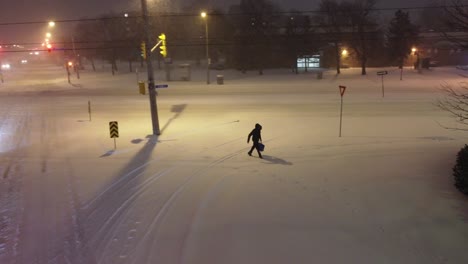 aerial drone pans to follow person walking across snowy landscape at night