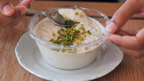 close up of a hand holding a spoon with a creamy dessert topped with pistachios