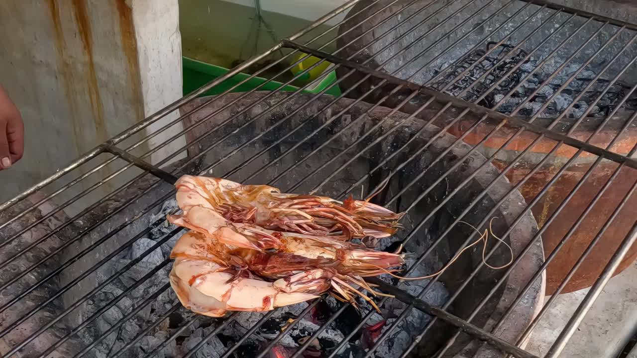 Tongs flipping shrimp over hot coals on a metal grill, showcasing detailed grilling techniques.