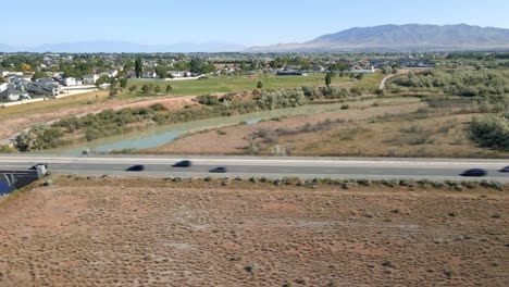 Cars-along-a-busy-street-in-Lehi,-Utah-near-the-suburbs-below-the-mountains---aerial-hyper-time-lapse