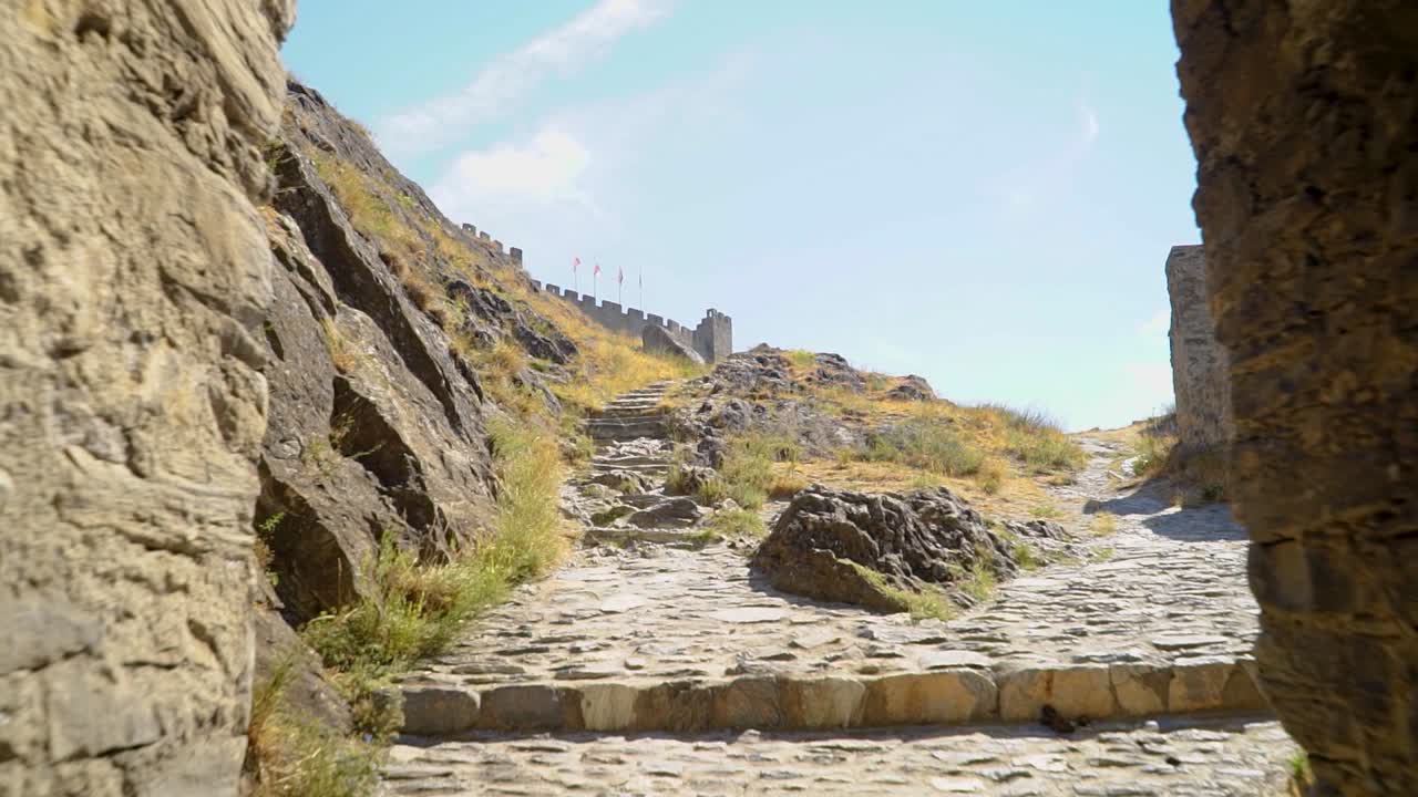 Forward dolly shot through stone arch in ancient castle wall ruins on summer day