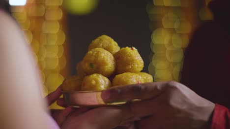 close up of man handing dish of ladoo to woman celebrating festival of diwali 1