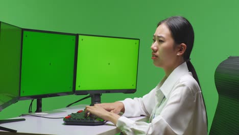 woman working on computers with green screen monitors