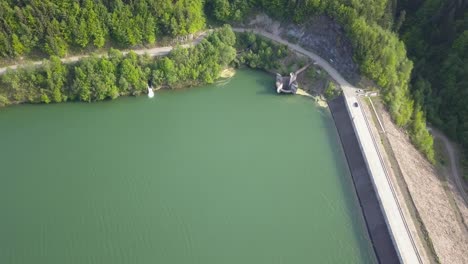 aerial downwards pan of lake-reservoir with road on the right of frame and car driving