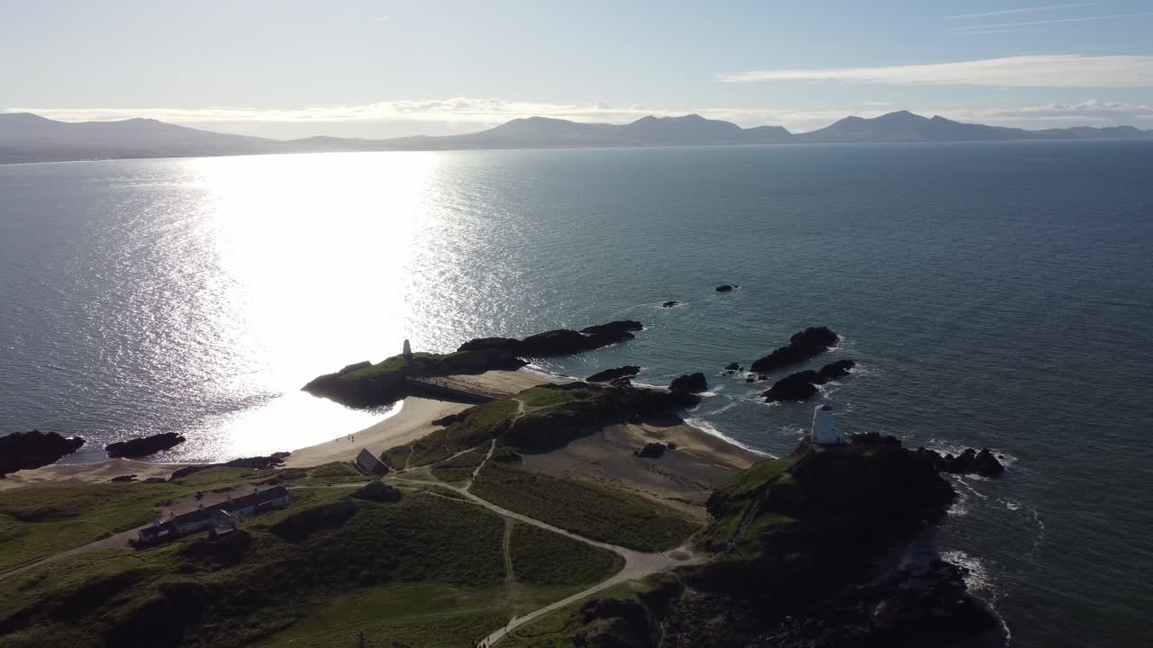 Aerial view Ynys Llanddwyn Welsh island with shimmering ocean and hazy Snowdonia mountain range across the sunrise skyline