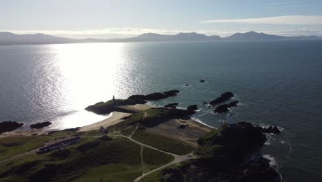 Vista-Aérea-De-La-Isla-Galesa-De-Ynys-Llanddwyn-Con-Un-Océano-Brillante-Y-Una-Nebulosa-Cordillera-De-Snowdonia-A-Través-Del-Horizonte-Del-Amanecer.