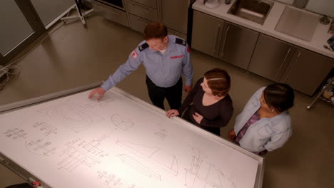 three people discussing diagrams on a large whiteboard