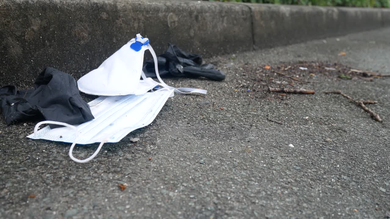 더럽게 버려진 사용된 코로나 바이러스 마스크와 장갑 복사 공간 돌리가 왼쪽 바람에 부는 거리에 쓰레기