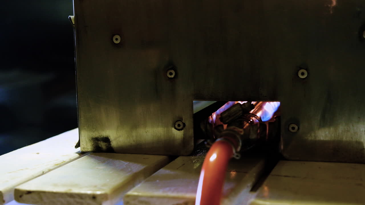 Gas pipe with flame inside stainless steel smoker on table, close-up