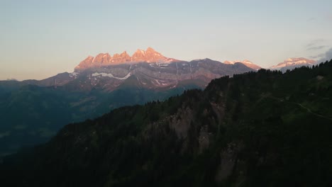beautiful sunset drone flight in the swiss alps. drone pans behind the tree line looking at the pink sunset on the peaks of the dents du midi in the val d'illiez of canton valais in switzerland.