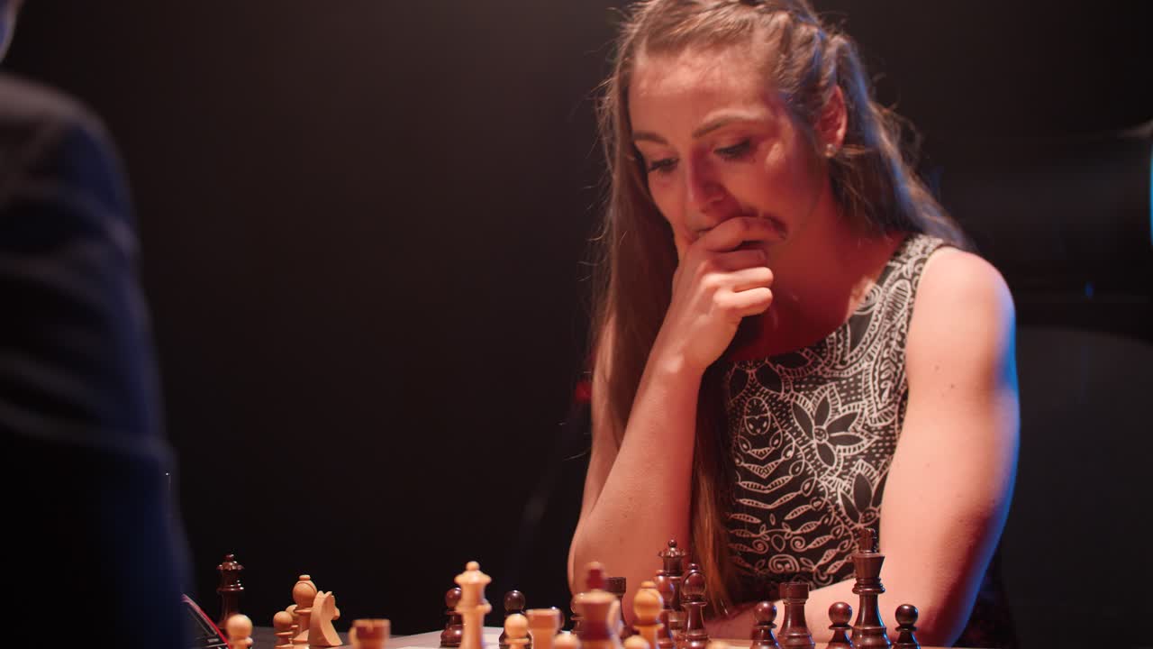 Young woman thinks and makes her next move in intense chess match against man- low key