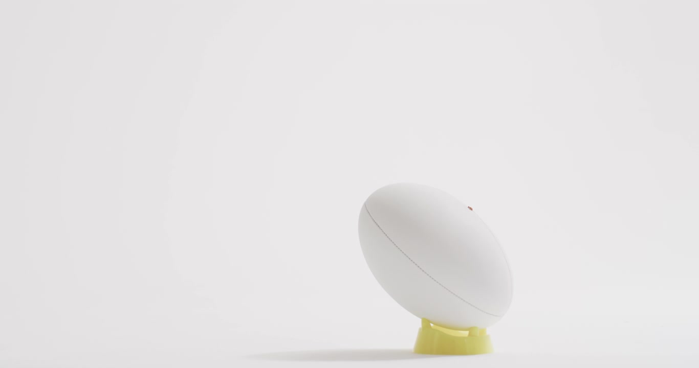 White rugby ball on kicking tee on white background with copy space, slow motion