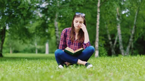 Attraktive-Studentin,-Die-Ein-Buch-Im-Park-Liest,-Sitzt-Auf-Dem-Rasen-HD-Video