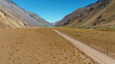 drone slow motion rearview descends to car traveling through dry golden desert in south america’s cajon del maipo region