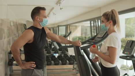 joven atleta mujer y hombre con mascarilla hablando en el gimnasio. deporte durante la pandemia de covid-19.