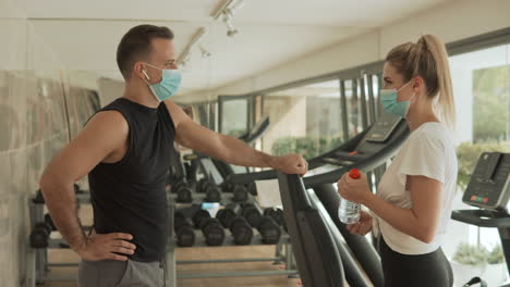 young athlete woman and man with face mask talking in the gym. sport during the covid-19 pandemic.