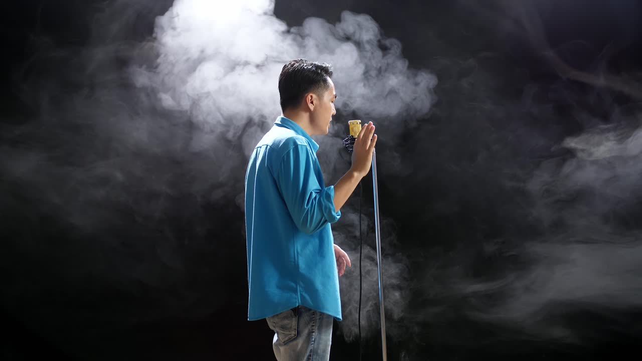 연기가 가득 찬 스튜디오 에서 마이크 로 노래 하는 남자
