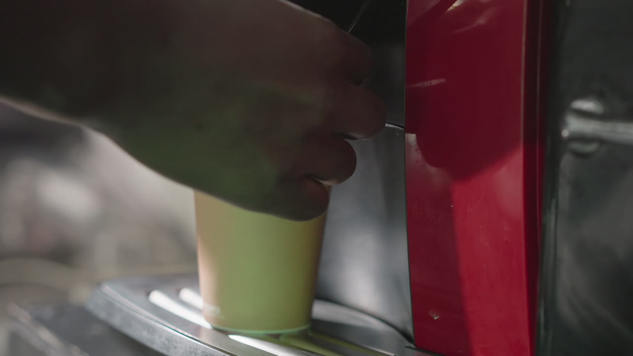 Close-up of hand placing cup onto coffee machine's drip tray, preparing to brew coffee, with focus on appliance use and precise placement in home or office kitchen environment