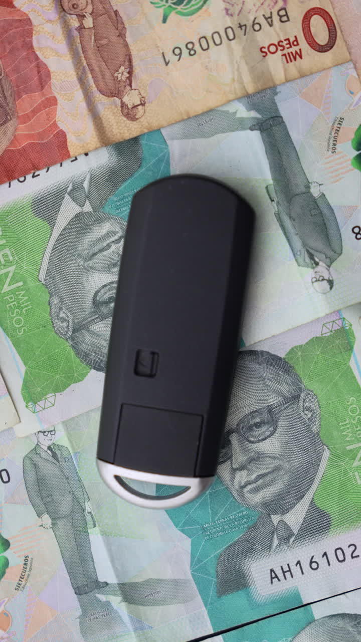 Detailed close-up shot of a car key placed on an arrangement of Colombian pesos. Captured in vertical video format, this composition highlights the textures and colors of currency