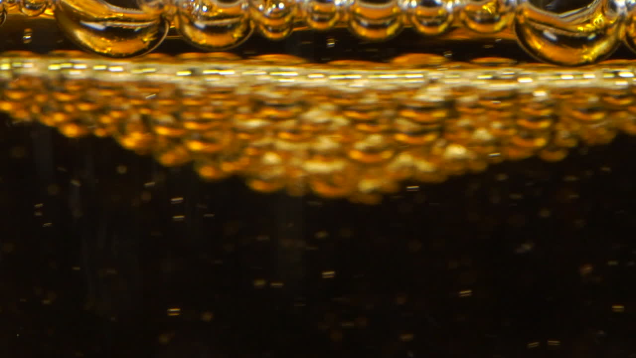 Grandi bolle che turbinano sulla superficie di un bicchiere in un liquido giallo come birra, sidro o limonata