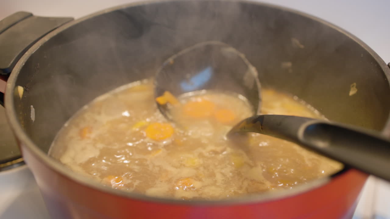 Pentola rossa che bolle carote e altre verdure in una zuppa avvolta nel vapore