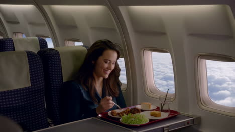 a woman enjoys an inflight meal on an airplane with a view of the clouds