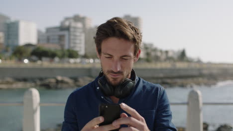 portrait of attractive young man using smartphone texting on sunny beachfront