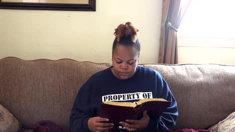Wideview-Einer-Afroamerikanischen-Frau,-Die-Bibel-Liest,-Während-Sie-Auf-Der-Couch-Faulenzt