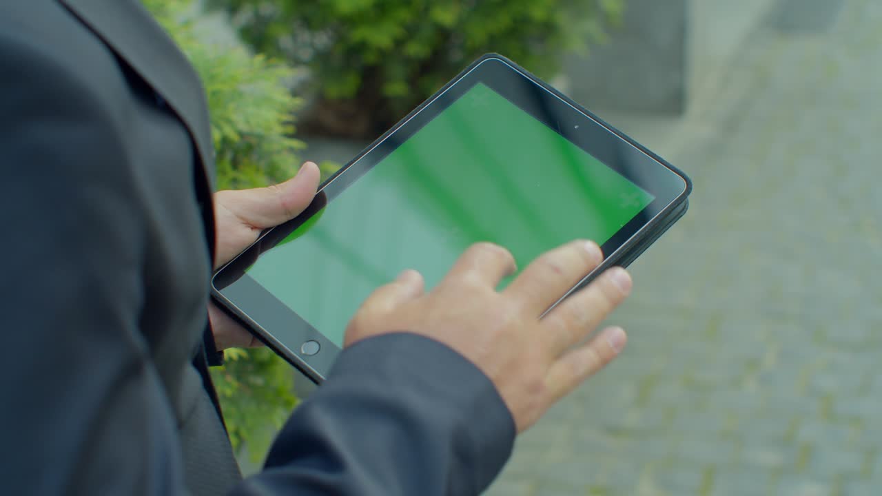hombre de negocios navegando por internet en línea en una tableta digital al aire libre. hombre de negocios de cerca trabajando en el touchpad en la calle. manos masculinas escribiendo en el pad con pantalla verde en cámara lenta.