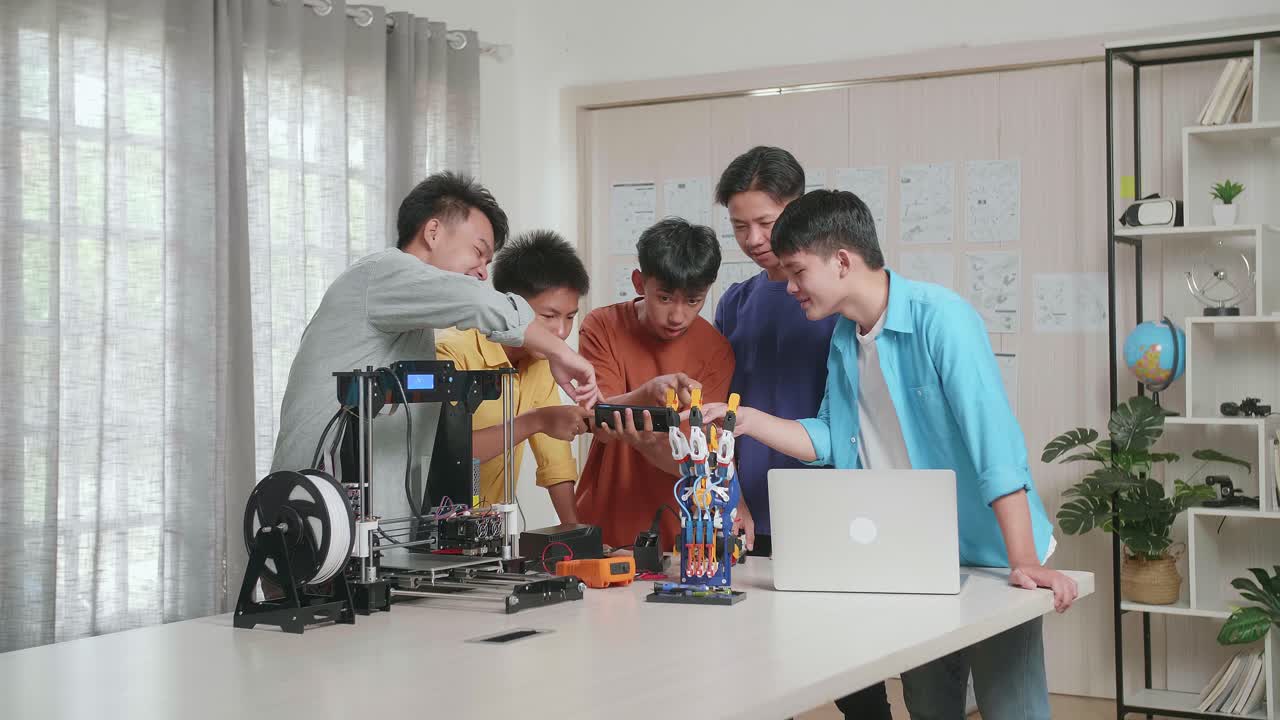 노트북과 3d 프린팅을 가진 젊은 아시아 소년 그룹이 집에서 일하는 동안 스마트 폰의 사진과 사이보그 손을 비교합니다.