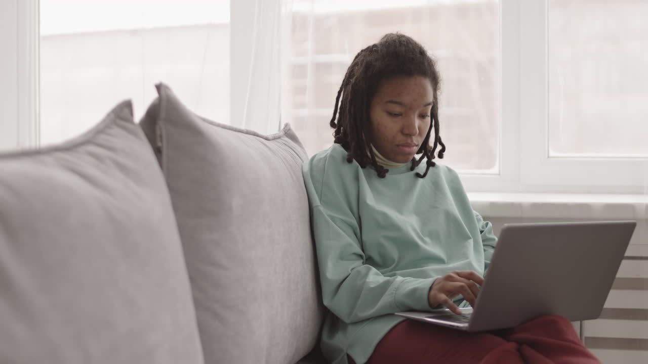 Young African Woman Sitting on Couch with Laptop