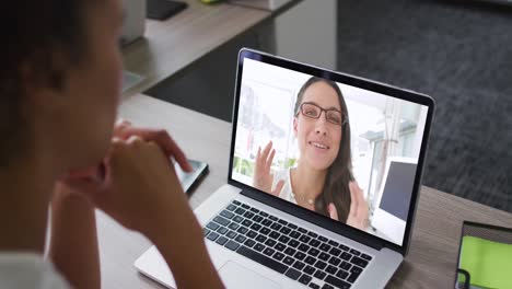 sección media de una mujer afroamericana haciendo una videollamada en una computadora portátil con una colega en la oficina