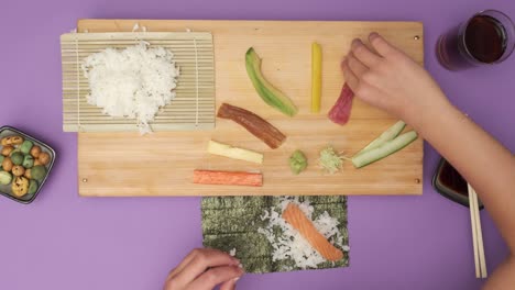 Draufsicht-Von-Zwei-Händen,-Die-Sushi-Auf-Einem-Violetten-Tisch-Zubereiten