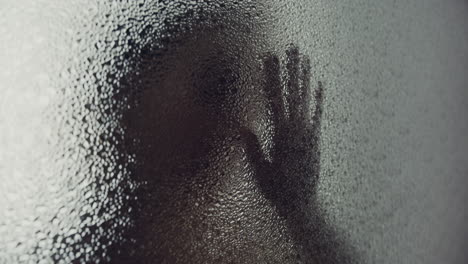 a female silhouette behind the frosted window touches the glass slowly