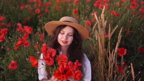 portrait-of-a-beautiful-dark-haired-girl-in-a-field-of-wildflowers-and-red-poppies,-wearing-a-hat-and-a-dress,-holding-a-bouquet-of-flowers-and-smiling-near-wheat-stalks