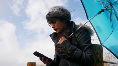 a woman in windy, stormy weather has her blue umbrella blown inside out as she laughs and smiles in a good mood