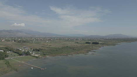 drone shot flying over shkodra lake in albania with mountains in the background and green plants grass nature underneath on a sunny day with haze above the lake log